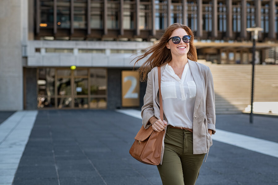 woman in green pants, white shirt, and cardigan walking in front of building